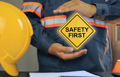 Worker in safety gear holding a 'Safety First' sign near a yellow helmet.