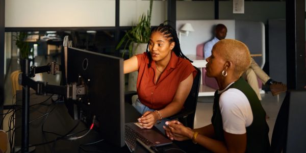 Two women working together at a computer in an office.