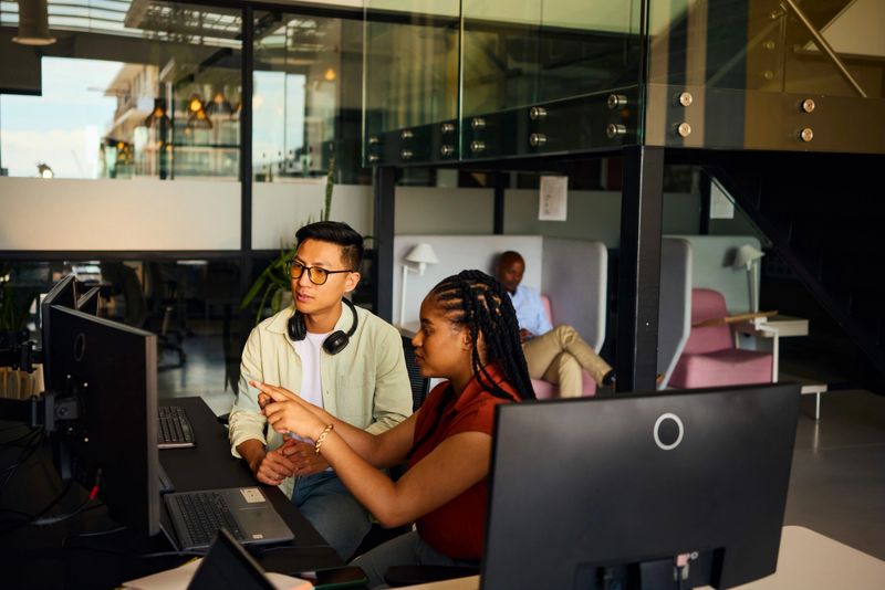 Two diverse software engineers working together, analyzing code on computer screens in a bright, modern office environment