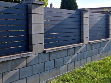 Modern fence with concrete blocks and horizontal slats casting shadows on grass.