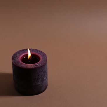 A lit dark purple candle casting a shadow on a brown surface.