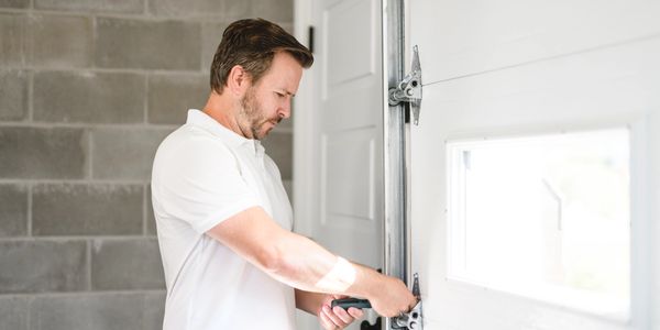 Man fixing garage door with a screwdriver in a bright room.