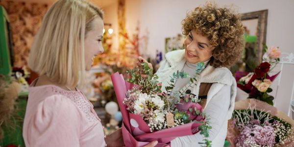 Two women exchanging a bouquet of flowers in a shop.
