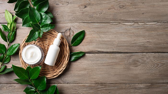 Natural skincare products with green leaves on wooden background.