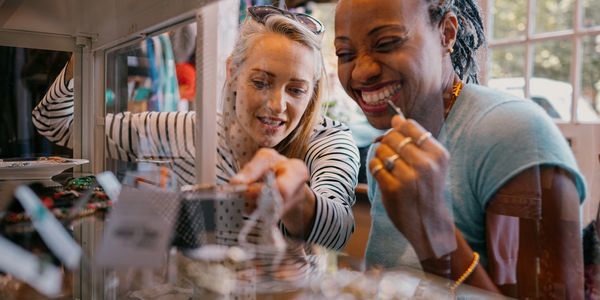 Two women happily browsing jewelry in a store display case.