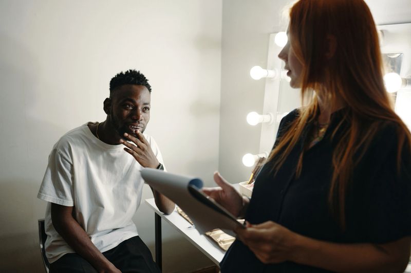 African American actor and Caucasian director engaging in an intense discussion about upcoming scene. Warm lighting from dressing room mirror reflecting on both participants