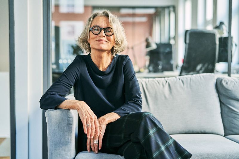 Portrait of a confident senior businesswoman sitting on a sofa in an office lobby, looking at the camera with a warm and professional smile