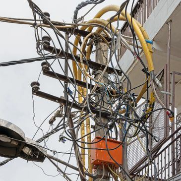 A chaotic cluster of electrical wires and cables tangled on a utility pole.