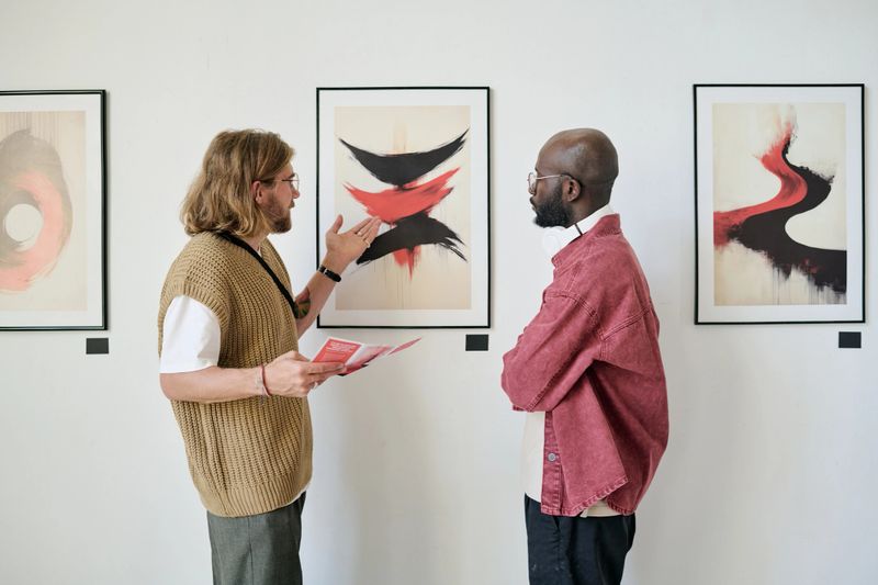 Two men talking and analyzing abstract artwork in modern gallery setting. They are paying close attention to the details and discussing perspective techniques