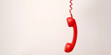 A red retro telephone handset hanging by its coiled cord.