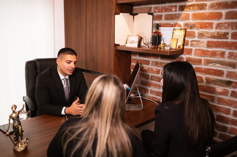 A lawyer holds legal documents while engaging in a discussion with clients in his office. The professional setting, combined with attentive conversation, reflects a focused consultation as they go over important case details.