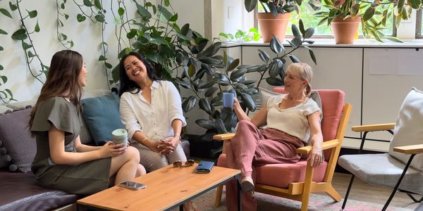 Three women chatting and relaxing indoors with drinks.