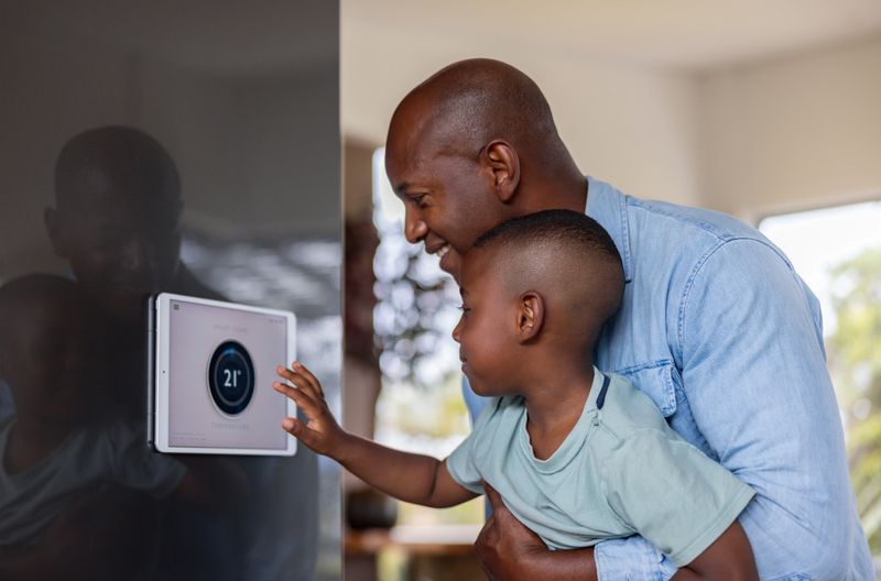 African American father and son using a home automation system to lower the temperature of their house