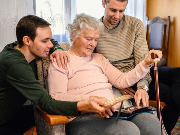 Two men and an elderly woman look at a photo album together.