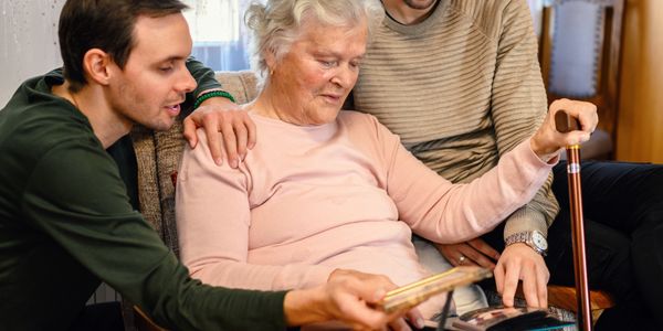 Elderly woman with two men looking at a photo album together.