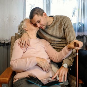 An elderly woman kisses a younger man on the cheek as they share a tender moment.
