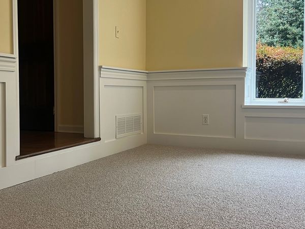 Empty room corner with beige carpet and natural light from a window.