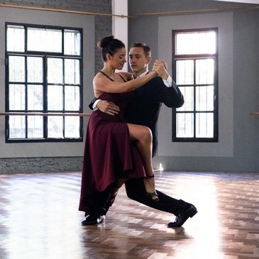 A couple elegantly dancing tango in a spacious studio with large windows.
