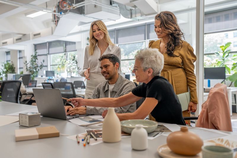A group of diverse entrepreneurs gathered around a laptop, engaged in a collaborative discussion about innovative ideas. The modern workspace fosters creativity, teamwork, and a dynamic exchange of insights.