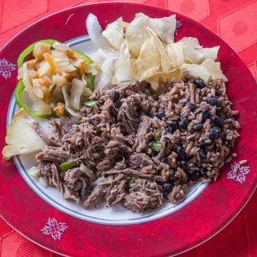 Plate with shredded beef, rice and beans, chips, and vegetable salad on a red tablecloth.