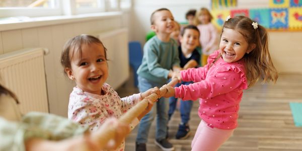 Children happily playing tug-of-war indoors at school.
