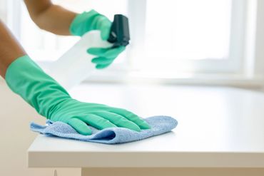 Person wearing green gloves cleaning a white surface with a blue cloth and spray bottle.