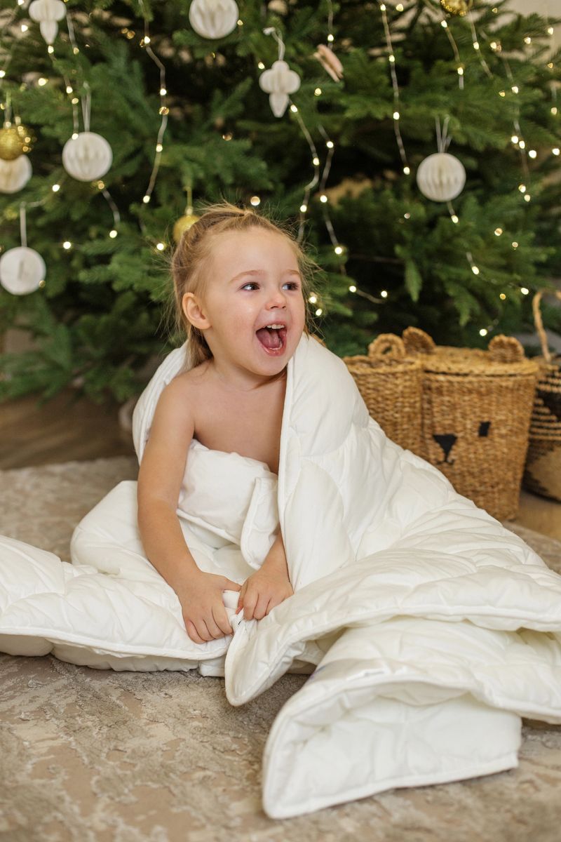 Joyful child celebrates Christmas morning, wrapped in warm blanket. TScene captures excitement of holiday season with decorated tree and festive atmosphere.