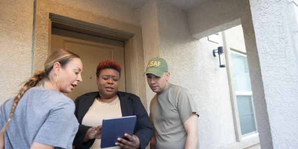 Three people looking at a tablet outside a building.