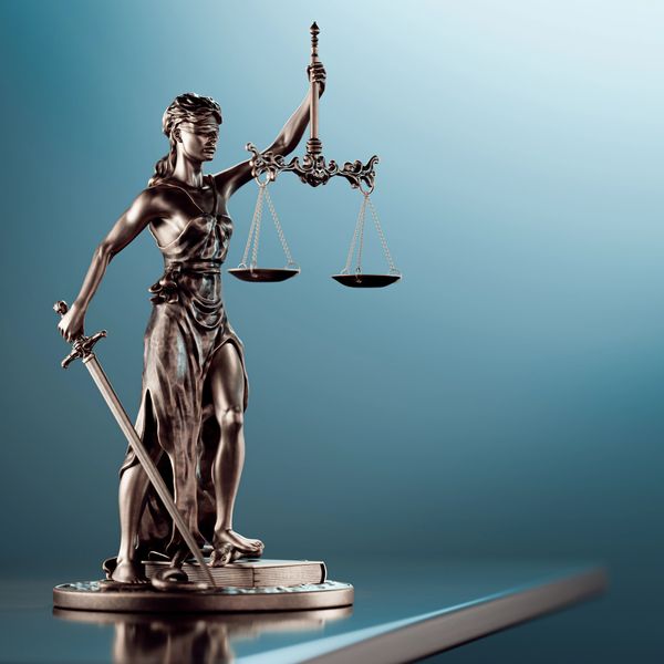Bronze statue of Lady Justice holding scales and sword, standing on a book.