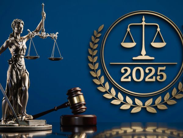 Statue of Lady Justice and a gavel on a desk with scales of justice and the year 2025 on the wall.