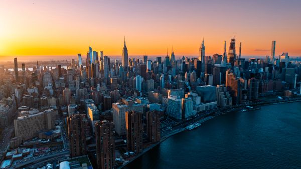 Aerial view of New York City skyline at sunset with water in foreground.