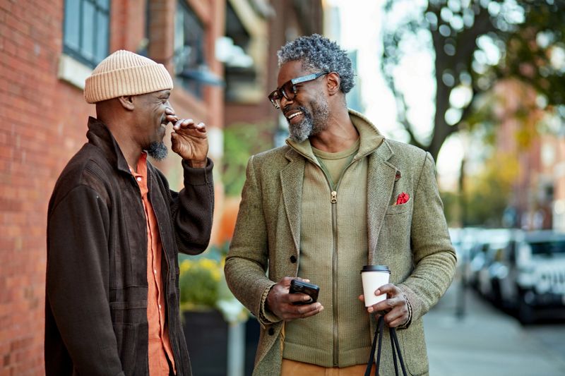 Waist up view of Black Chicagoans enjoying weekend leisure, pausing on city sidewalk to look at smart phone and react with amusement.