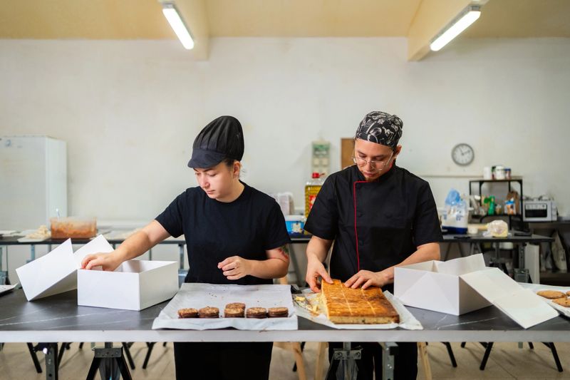 Two dedicated pastry chefs working in a bakery kitchen, carefully placing freshly baked cakes into boxes, getting ready for delivery or sale