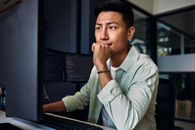 Young asian man working as software developer, coding on computer in modern office