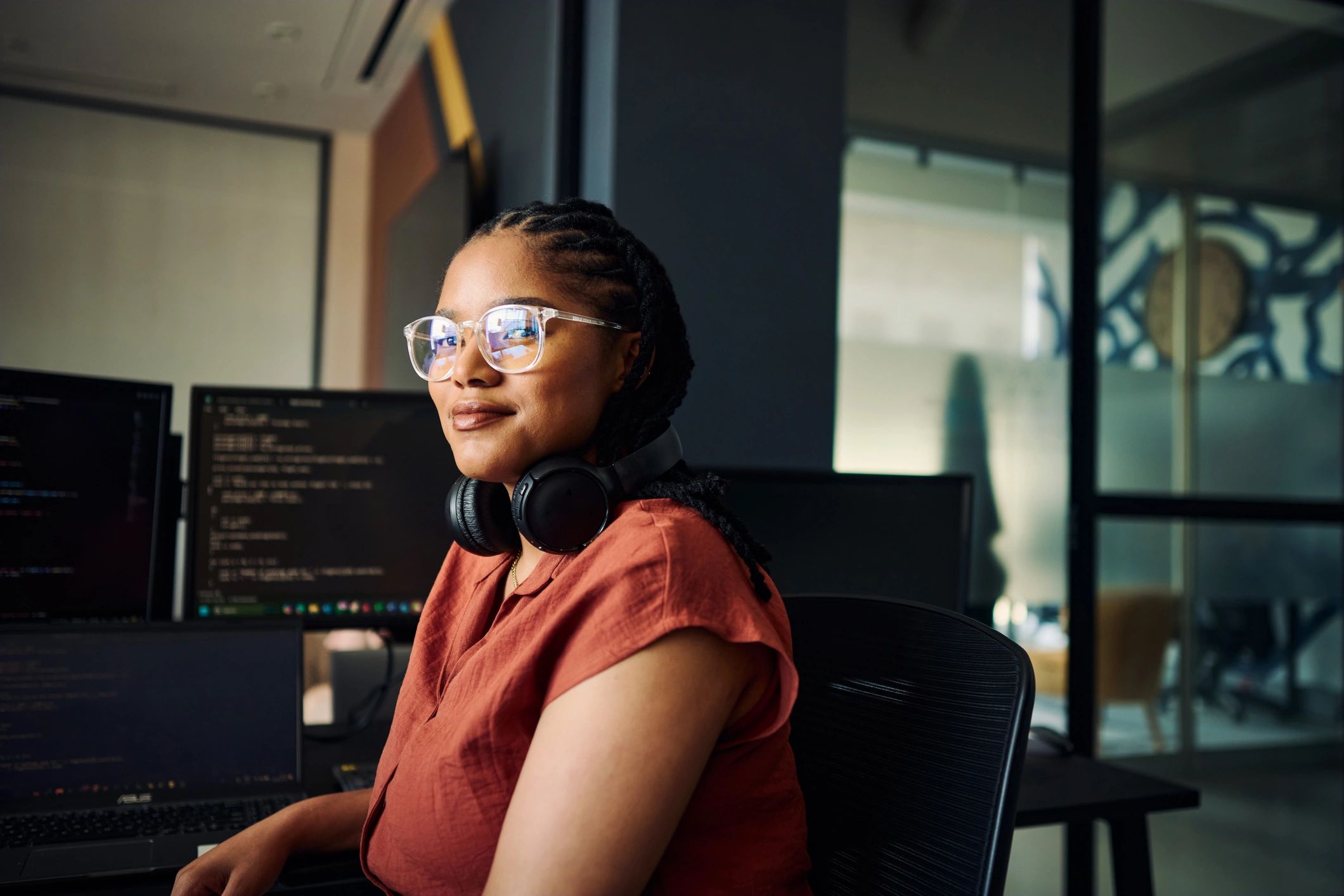 Confident woman with headphones and glasses working at a computer.