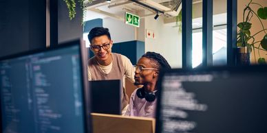Two developers collaborating in an office with code on screens.