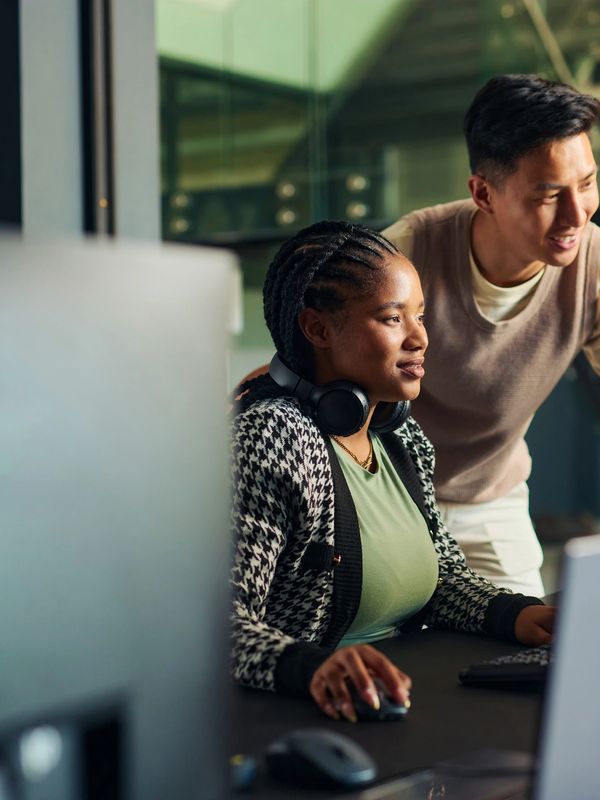 Two colleagues collaborate while working on a computer in a modern office.