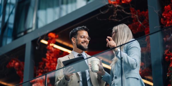Two professionals discussing work outdoors with a laptop and coffee.
