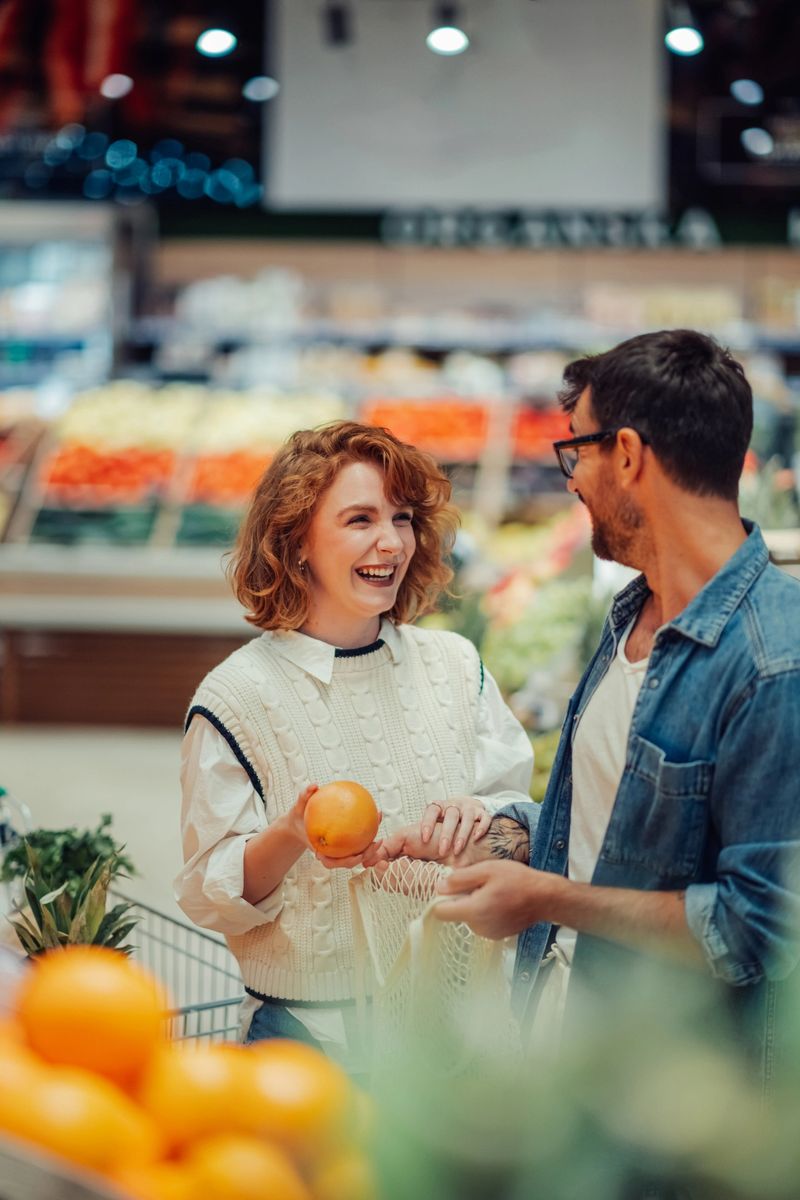Young couple happily shops for fresh produce at the grocery store, picking out oranges and sharing joyful moments together, embracing a sustainable lifestyle