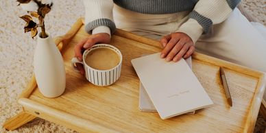 Person holding a coffee mug with a wedding planner on a wooden tray.