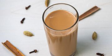 A glass of chai tea surrounded by spices on a white surface.