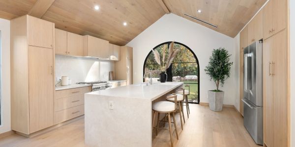 Modern kitchen with light wood cabinets and a large marble island under a wooden ceiling.
