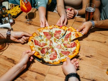 Des mains prenant des parts de pizza en groupe.