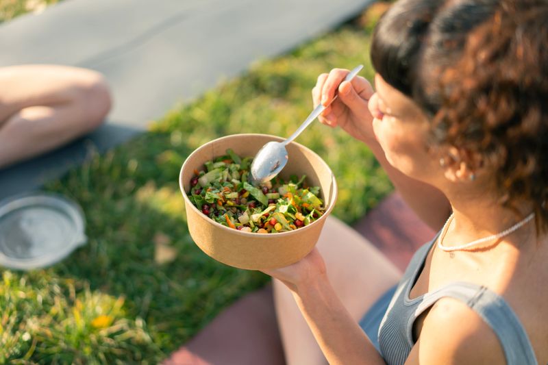 Young woman eating a fresh salad from a biodegradable container in a park after a yoga session