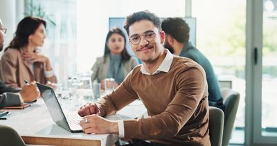 With flexible funding, a young man smiling at camera during a business meeting with colleagues.