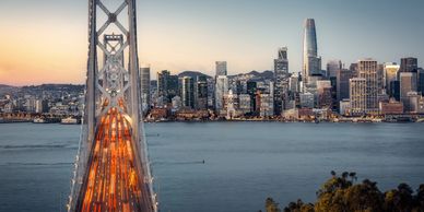 Bay Bridge leading to San Francisco skyline at dusk with light trails from traffic.