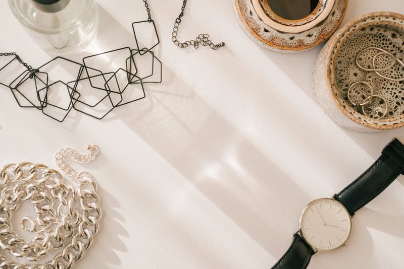 Women fashion feminine composition. Accessories and cup of coffee on a white beige background. Flat lay, top view, minimalistic trendy lifestyle collage. Coffee, watch,rings, chain, bracelet, perfume.