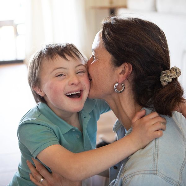 A mother lovingly kisses her smiling son with Down syndrome at home.