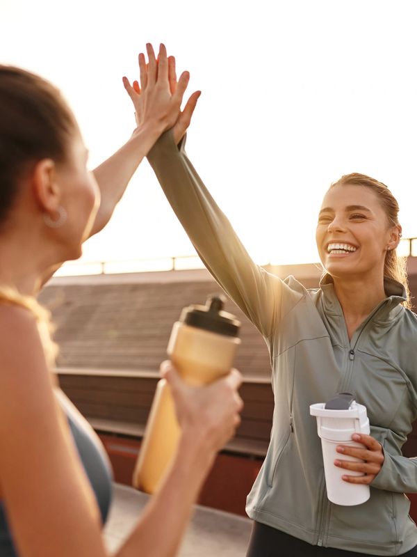 Two women high-fiving after a workout, holding water bottles and smiling.