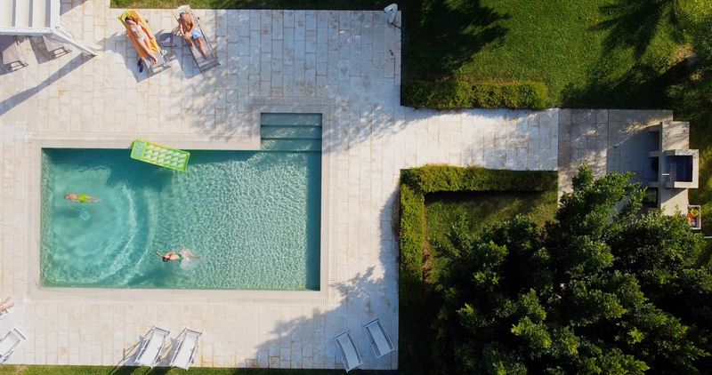 View of a beautifully designed swimming pool with lounge chairs and a lush, green landscaped background